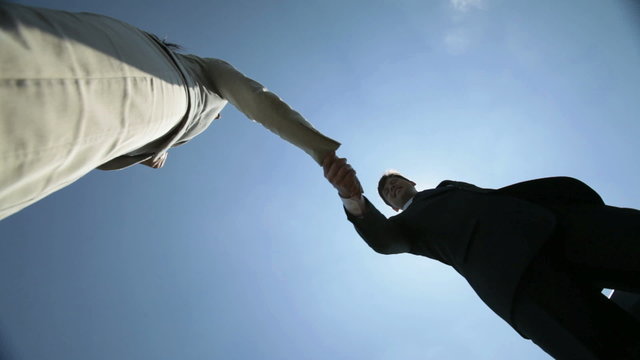 Low angle view of two colleagues greeting each other with handshake against clear sunny sky. Suitable for business, partnership and teamwork visuals