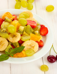 Fresh fruits salad on plate and berries on white wooden table