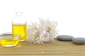 Chrysanthemum with massage oil and stones on bamboo mat
