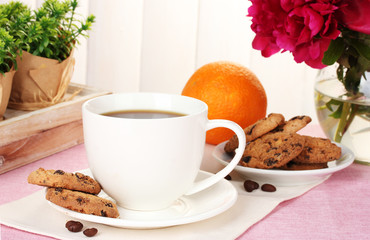 cup of coffee, cookies, orange and flowers on table in cafe