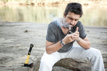 rough man standing by the river lighting up a cigarette - series