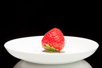 white saucer with red strawberr on a black background
