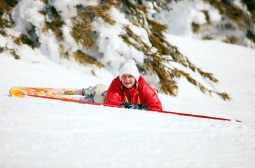 Cute young female skier looking at the camera after falling down
