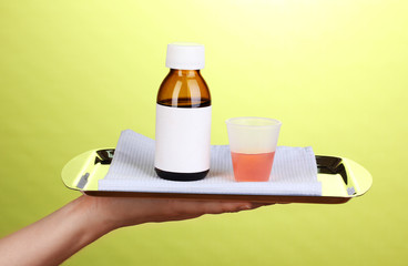 Hand holding tray with medicines on green background