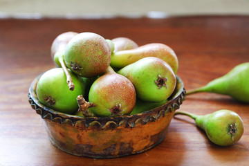 Small ripe pears in rustic clay dish on wooden table