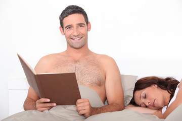 Man reading in bed as his partner sleeps