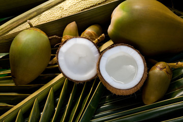 Whole and opened coconuts on palm leaf