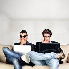 Two young gamers sitting together on sofa and using their laptop