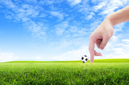 finger and soccer ball on green grass background