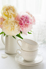 White cups and a bouquet of peonies on the table