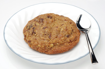 close up of oatmeal raisin cookie on white plate with spoon