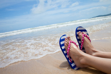 Young girl legs in colorful flipflop sandals on sea beach