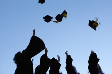 Five graduates throwing their hats in the sky