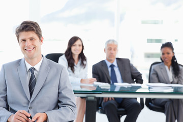 Smiling young businessman sitting in front of his team and looki