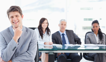 Fototapeta premium Smiling young executive sitting in front of his team with his ha