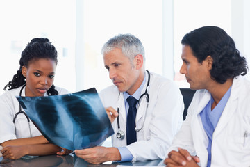 Fototapeta premium Mature doctor with two co-workers working on an x-ray of lungs