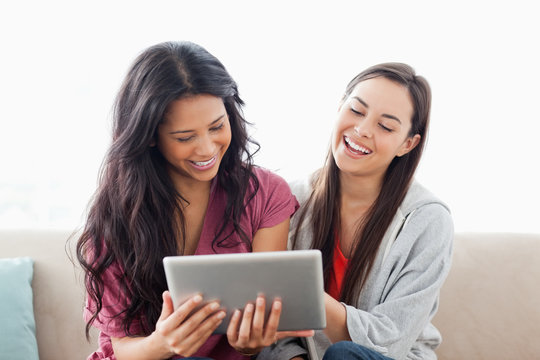 A laughing pair of women on the couch watching their tablet pc