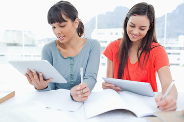 Two girls both using tablet pc's to do their homework