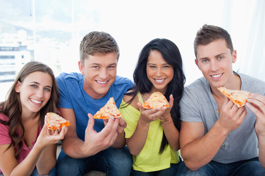 Friends about to eat their pizza as they look at the camera