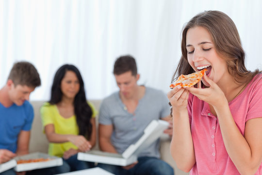 A woman about to eat a slice of pizza with her friends behind he