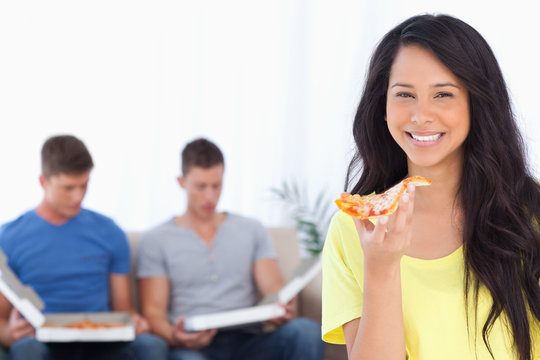 A woman holding pizza in her hand as her friends sit behind her