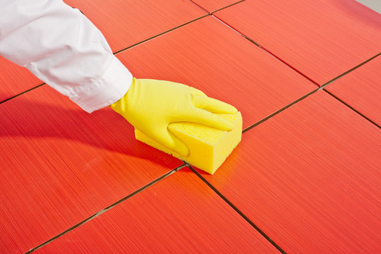 hand with yellow gloves and yellow  sponge clean red tiles