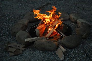 Lagerfeuer in Halbdunklen umrandet mit Findlingen als Brandschutz
