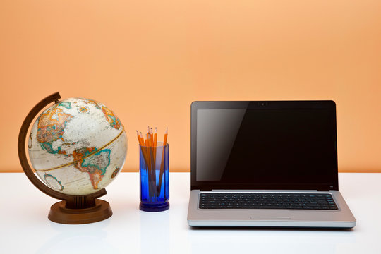 Students Desk With Globe, Pens And Laptop