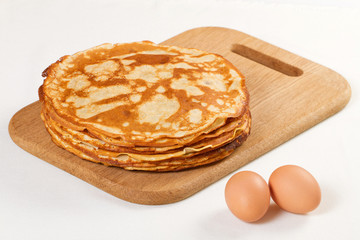 Pile of pancakes with some flour and eggs on white background