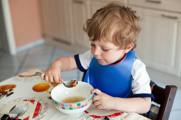 Adorable boy with blond hairs eating soup