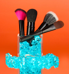 Make-up brushes in glass cup with stones on red background