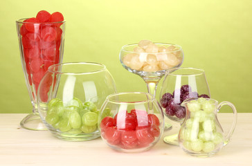 Color candies in glasses on wooden table on green background