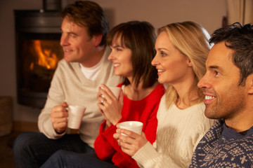 Group Of Middle Aged Couples Sitting On Sofa With Hot Drinks Wat