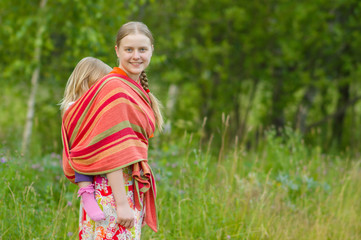 Young mother with daughter in wrap walking in park