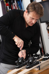 Sales Assistant Adjusting Fittings On Skis In Hire Shop