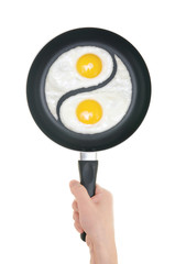 Fried eggs in the form of yin and yang on pan. Pan in hand on wh