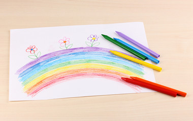 Children's drawing of rainbow and pencils on wooden background