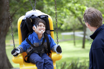Father pushing disabled son  on handicap swing - obrazy, fototapety, plakaty