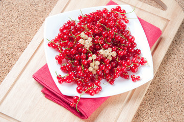 Glass plate full of red currant on a wooden board