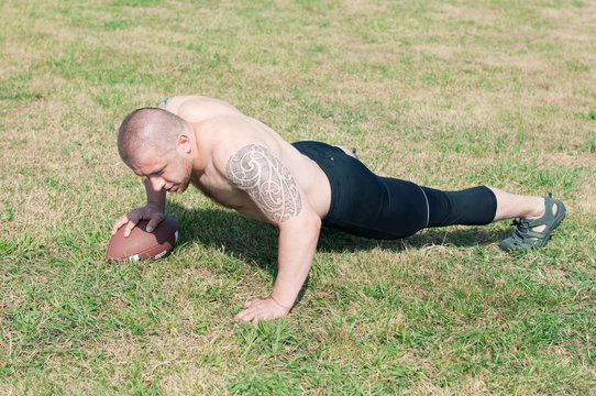 Shirtless american football player doing push-ups with ball