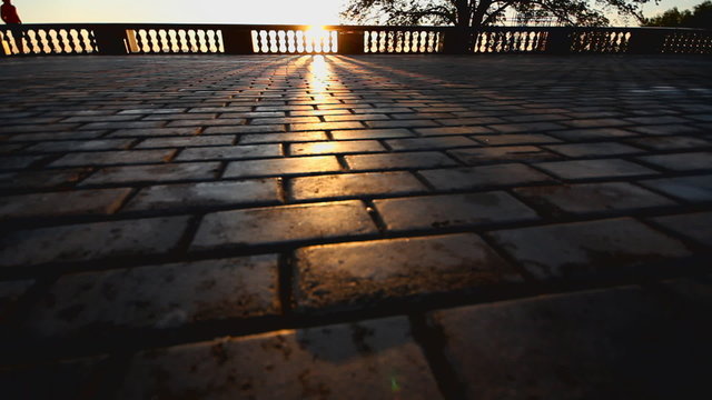 rays of sun over parapet on tile sidewalk