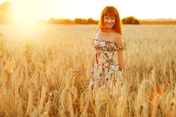 Obraz premium Young pretty woman with red hair at the field of wheat