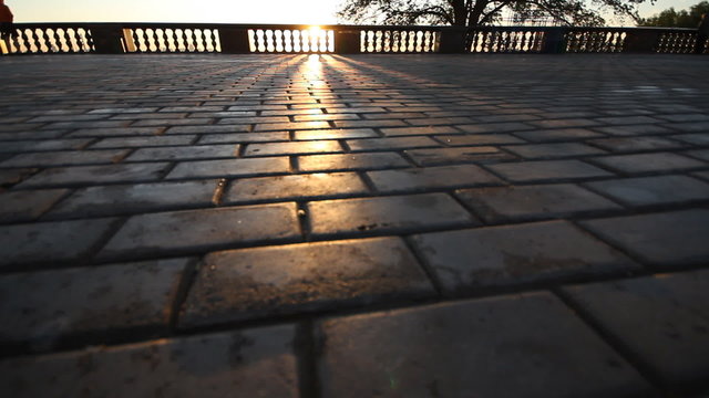 rays of sun over parapet on tile sidewalk