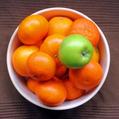 single Green apple in a bowl full of oranges