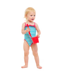 Baby girl in swimsuit holding bucket and shovel looking in corne
