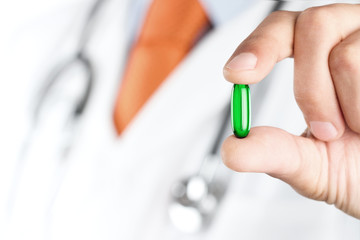 Close up of male doctor holding green pill