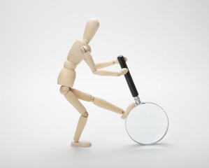 Wooden man with magnifying glass on white background
