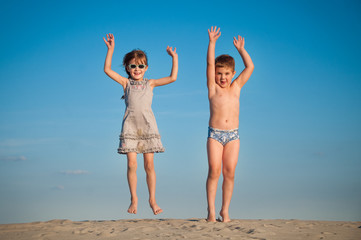 Photo of happy siblings jumping over sand