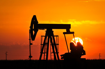 An oil pump jack is silhouetted by the setting sun