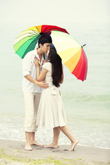 Fototapeta premium Couple kissing under umbrella at the beach